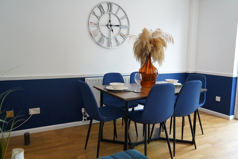 Modern dining room with blue chairs, wooden table, wall clock and pampas grass decoration