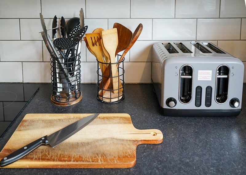 Kitchen countertop with utensil holders, wooden chopping board, knife, and toaster
