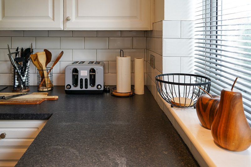 Modern kitchen with dark countertop, white subway tile backsplash, wooden utensils and appliances