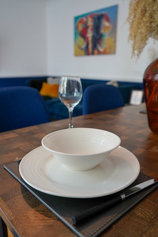 Dining table set with white plates, wine glass and cutlery, blue sofa background