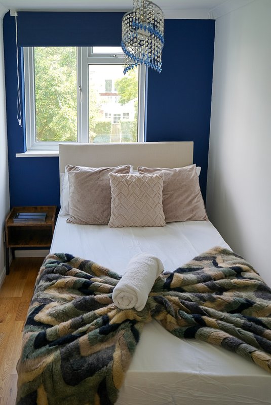Compact bedroom with double bed, navy accent wall, patterned cushions and fur throw