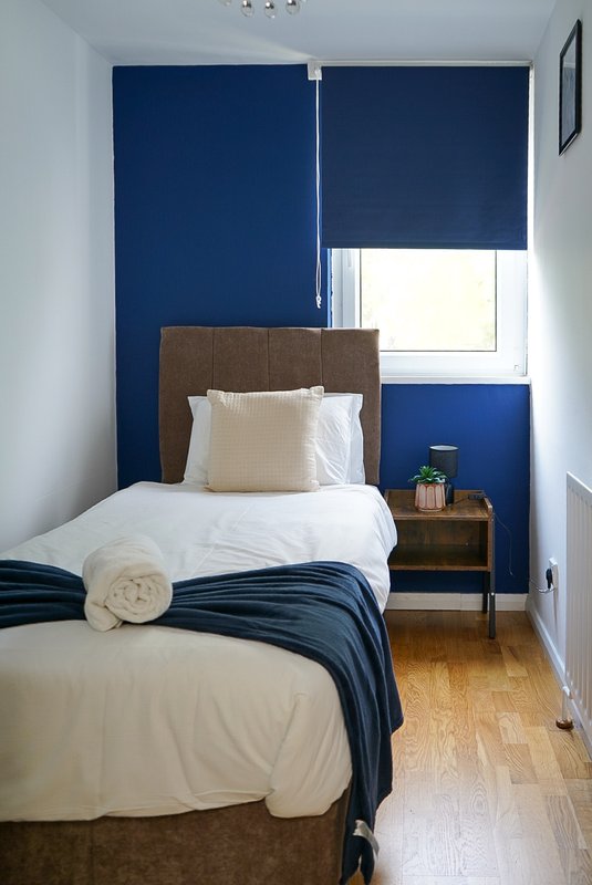 Modern bedroom with single bed, navy blue accent wall, wooden nightstand and hardwood floor