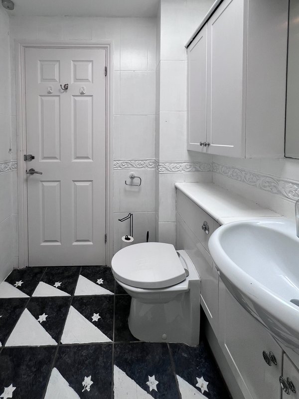 Clean bathroom with toilet, sink, mirror, shower enclosure and geometric patterned floor mat