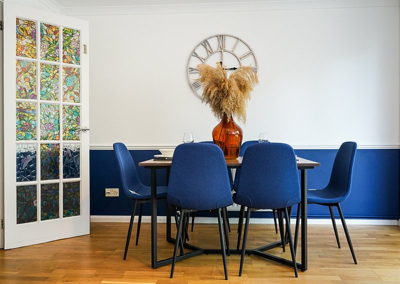 Modern dining room with blue chairs, round table, and decorative wall clock above vase