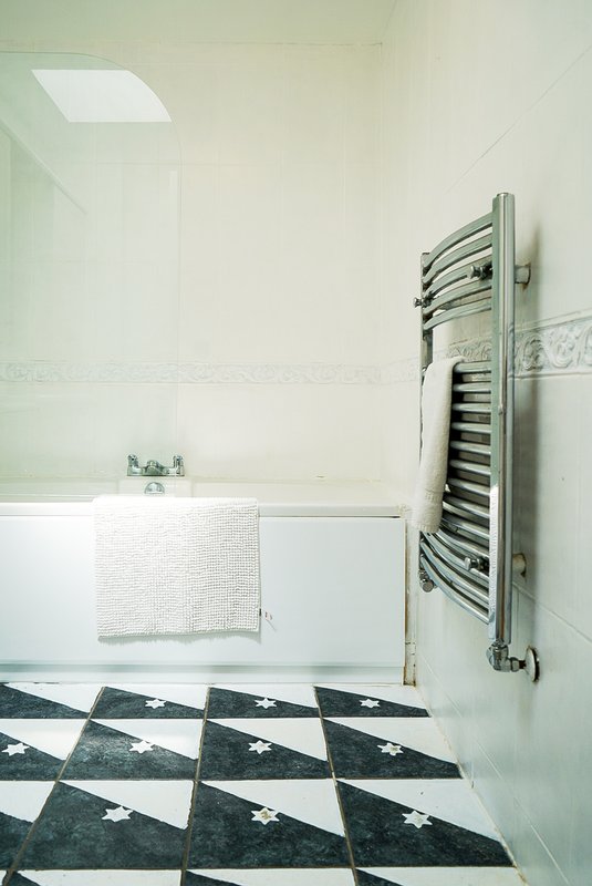 Modern bathroom with white bathtub, heated towel rail, black and white geometric floor tiles
