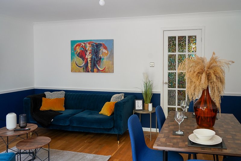 Living room with navy velvet sofa, colorful elephant artwork, wooden dining table and pampas grass decor