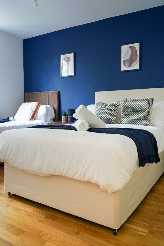 Modern bedroom with dual beds, blue accent wall, patterned cushions and wooden flooring