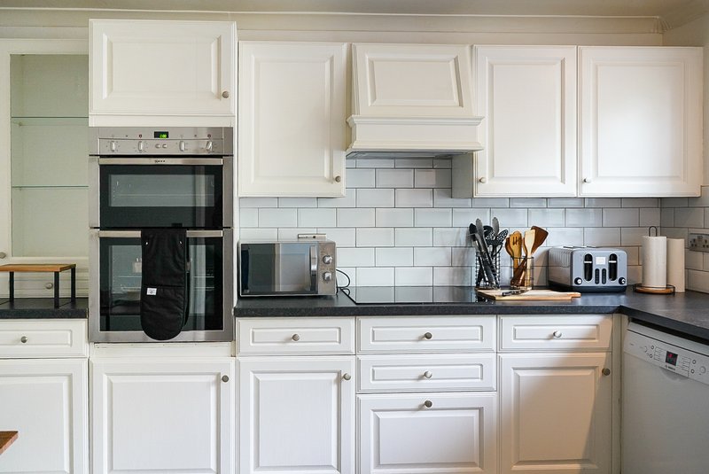Modern kitchen with white cabinetry, subway tile backsplash, black countertops and stainless steel appliances