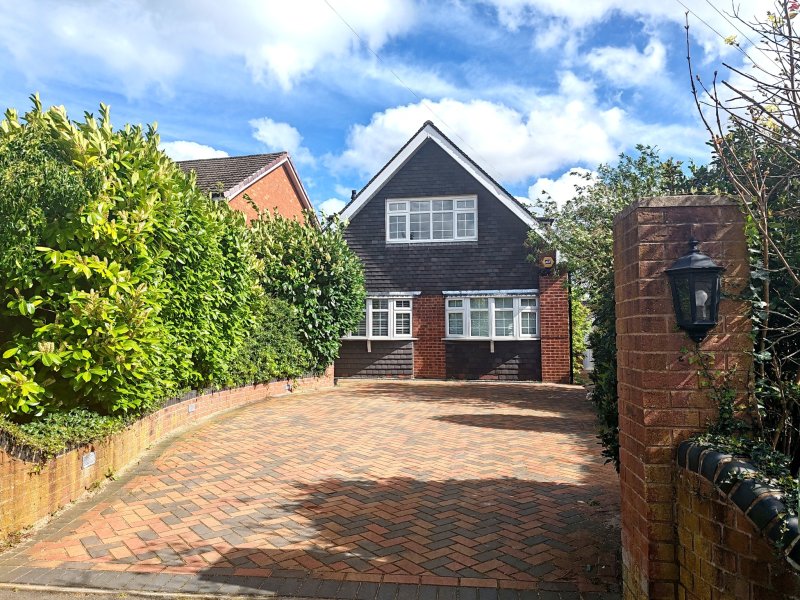 Brick detached house with large driveway, gabled roof, and surrounding garden hedges.