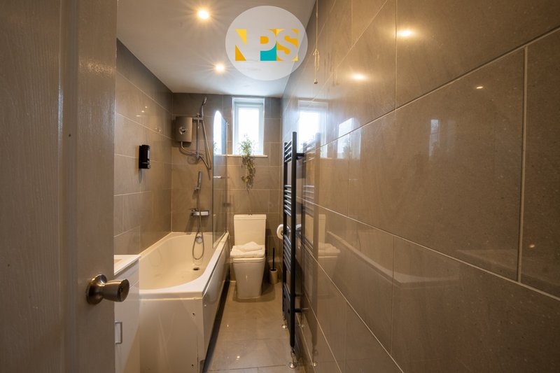 Modern bathroom with bathtub, toilet, shower enclosure and colourful ceiling light fixture.