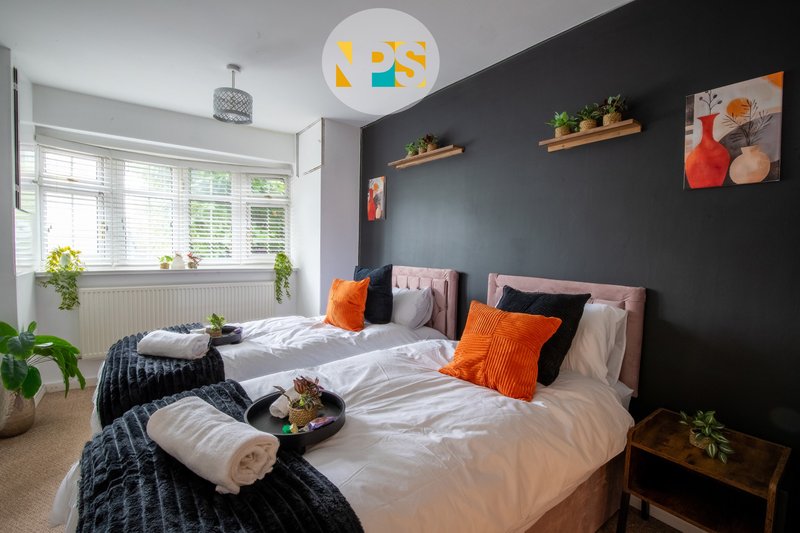 Modern bedroom with two single beds, dark feature wall, orange cushions and white ceiling light.