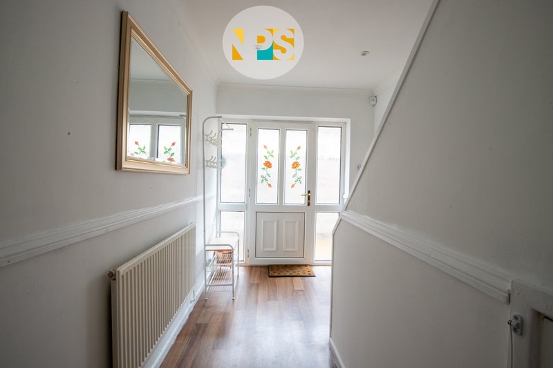 Bright hallway with white walls, wooden floor, radiator, framed mirror and ceiling light fixture.