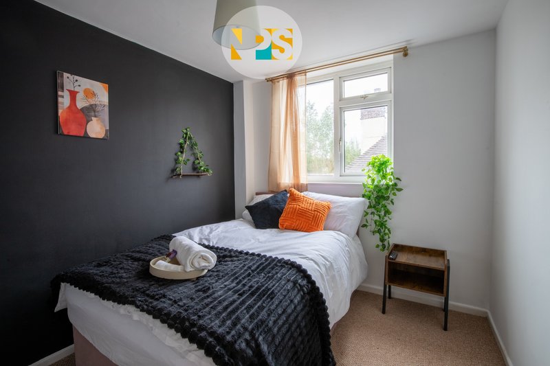 Modern bedroom with double bed, dark accent wall, colourful ceiling lamp and window with curtains.