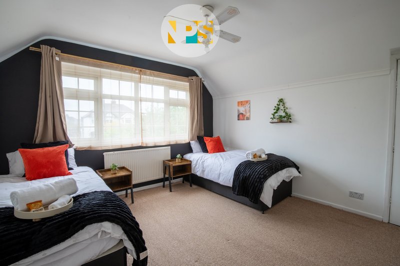 Bedroom with two single beds, large window with curtains, ceiling fan and light fixture.