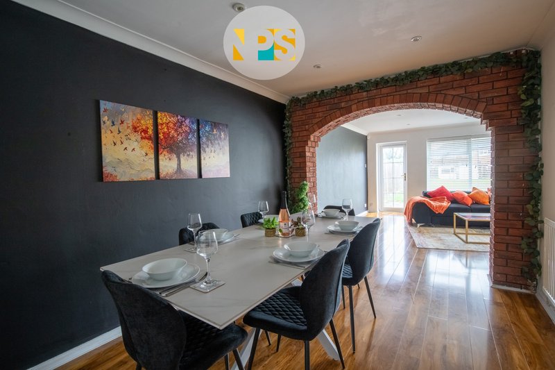 Modern dining room with white table, black chairs, exposed brick archway and artwork on dark walls.