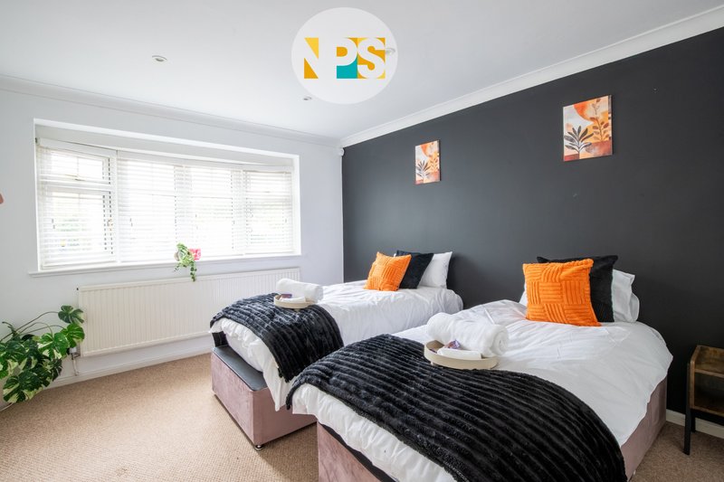 Modern bedroom with two single beds, dark feature wall, orange cushions and white ceiling light.