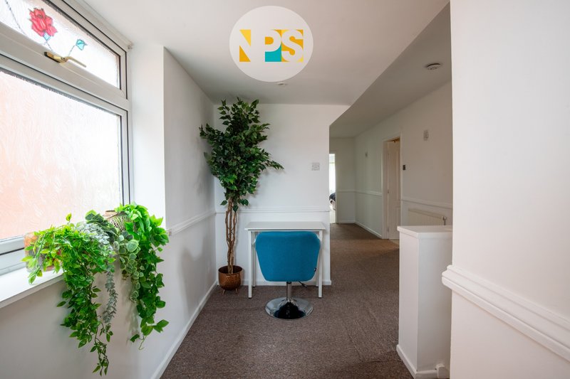 Bright hallway with potted plants, blue chair, colorful ceiling light, and white doors