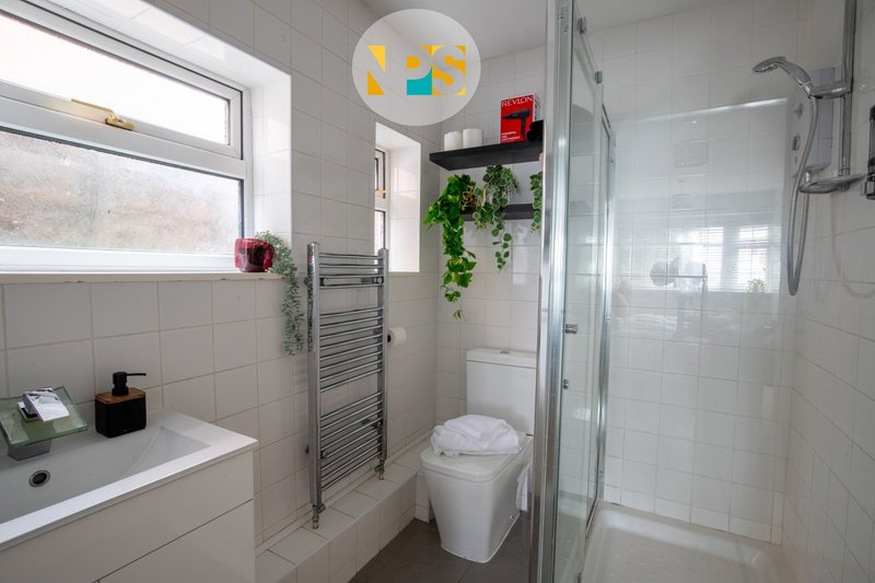 Clean modern bathroom with white tiles, sink, toilet, shower enclosure and window.