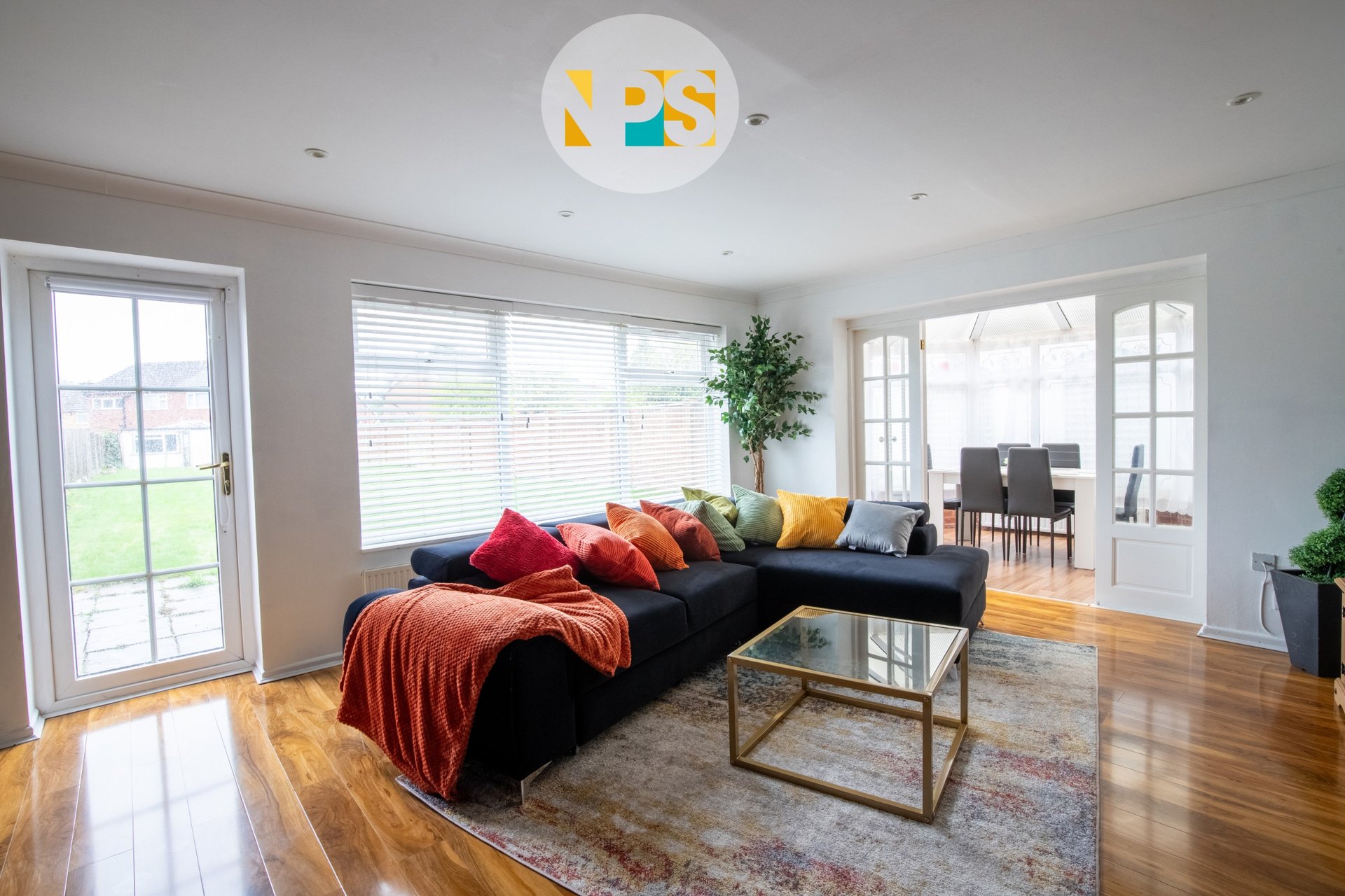 Spacious living room with black sectional sofa, colorful cushions, wooden floors and natural light from large windows