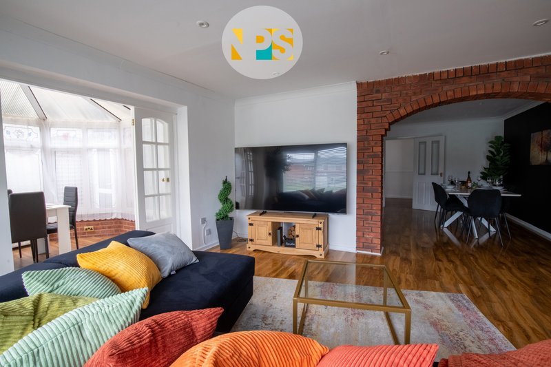 Living room with colourful cushions, sofa, 75-inch Smart TV, wooden floor and exposed brick wall.