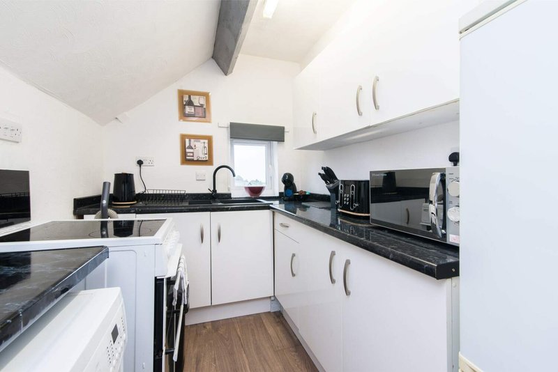 White kitchen with black countertops, appliances, and wooden flooring throughout