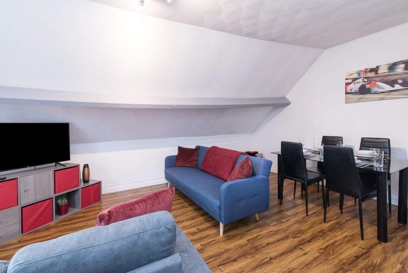 Modern living room with blue sofa, red cushions, wooden floor and dining area