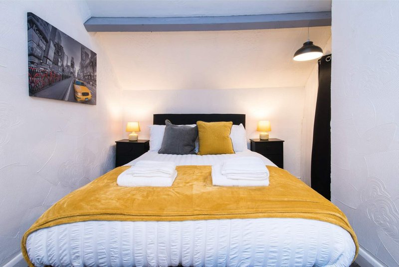 Compact bedroom with double bed, yellow throw, black headboard, bedside lamps and wall art