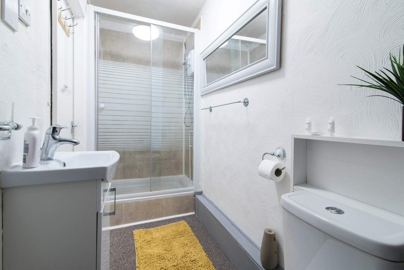 Clean modern bathroom with white sink, glass shower enclosure, yellow bath mat