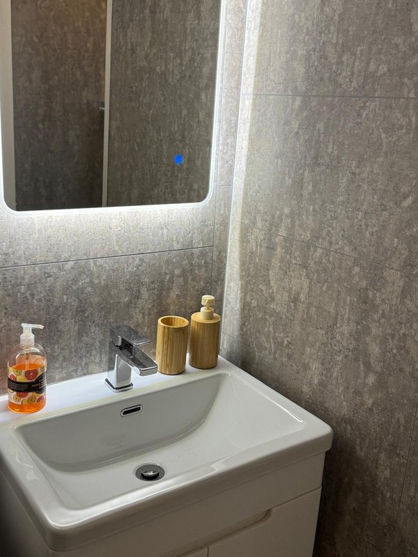 Modern bathroom with white sink, illuminated mirror, grey tile walls and toiletries