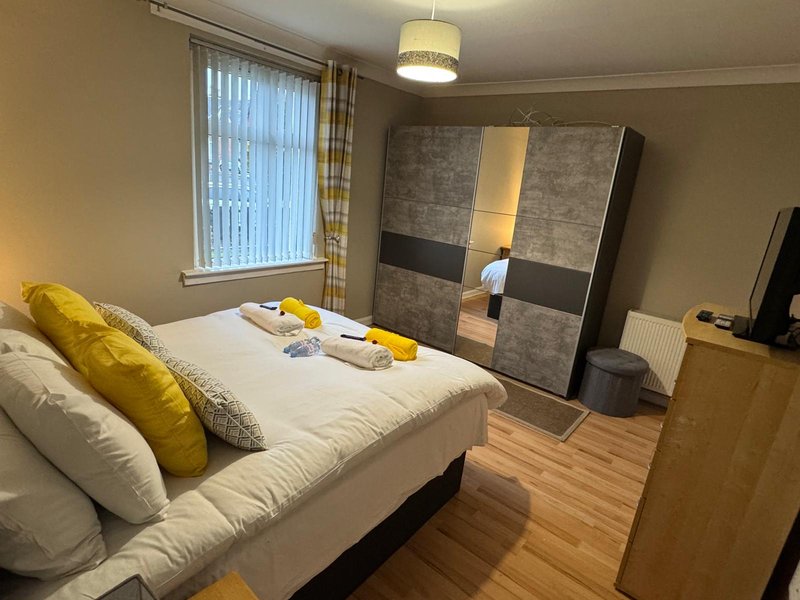 Bright bedroom with double bed, yellow cushions, wooden wardrobe and window with blinds