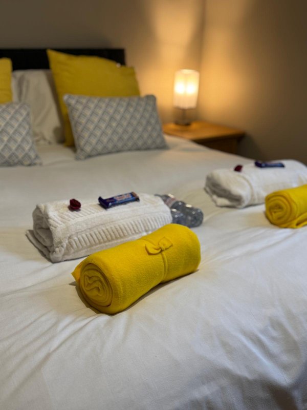 Bedroom with double bed, yellow and white rolled towels, patterned pillows, and bedside lamp