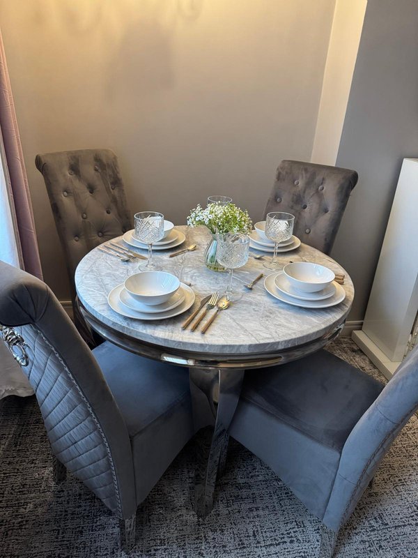 Dining table set for four with white plates, gold cutlery and fresh flowers centerpiece