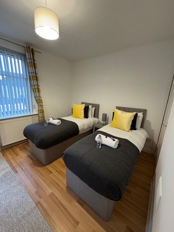 Bright bedroom with two single beds, yellow cushions, wooden floor and pendant light