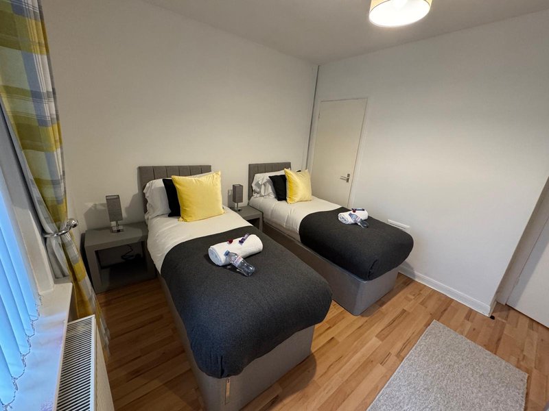 Twin bedroom with two single beds, yellow cushions, wooden flooring and ceiling light