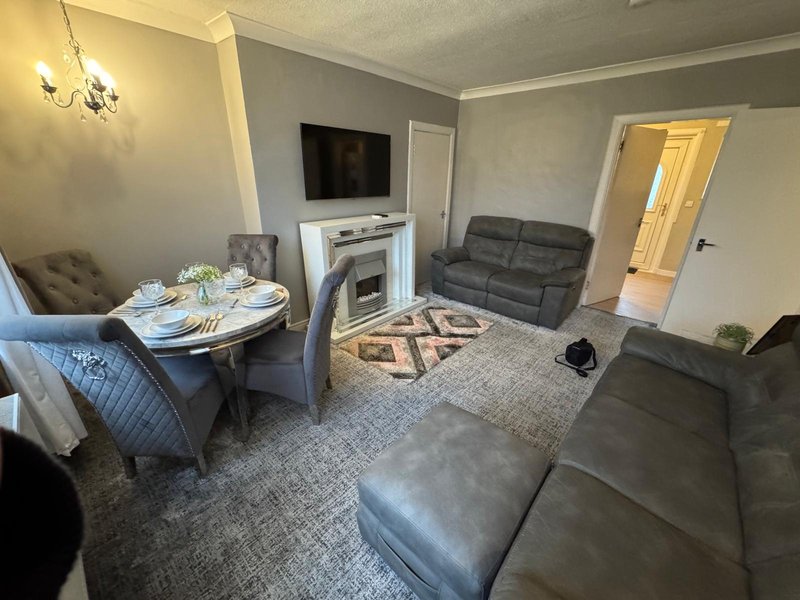 Living room with grey sofas, fireplace, dining table, wall-mounted TV and neutral décor
