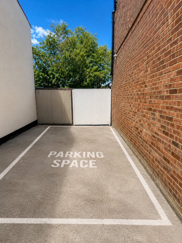 Empty parking space with white line markings, brick wall, and blue sky beyond