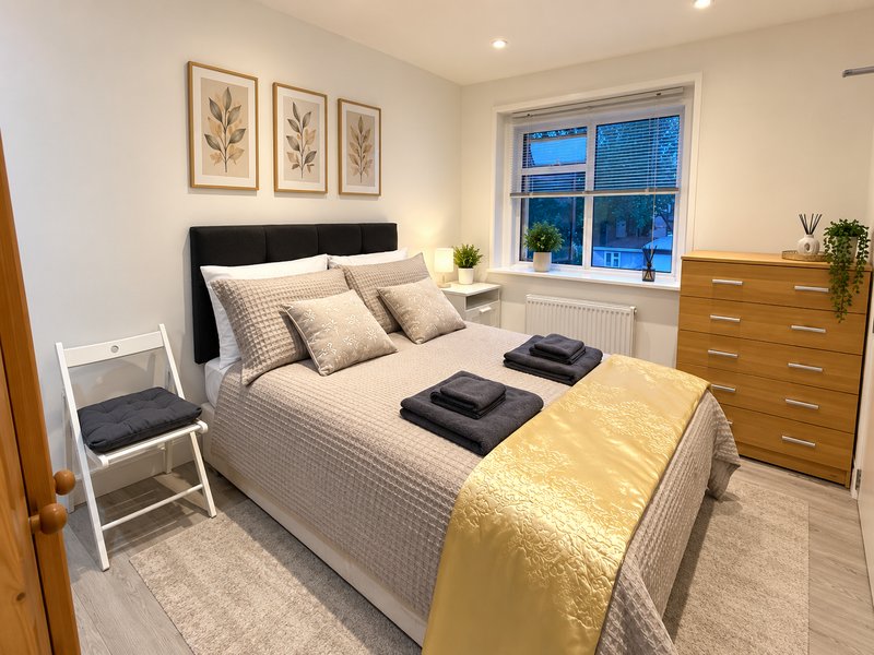 Modern bedroom with double bed, black headboard, wooden dresser and framed botanical wall art