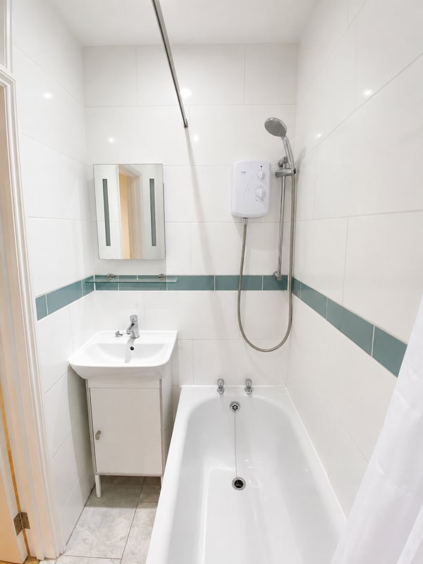 Compact bathroom with white subway tiles, green stripe trim, sink, bathtub and shower head