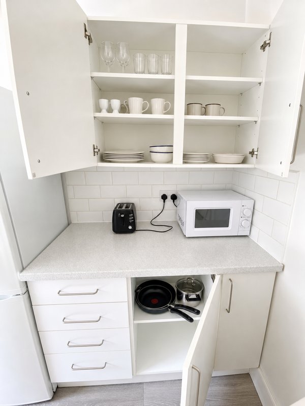 Compact kitchen with white cabinetry, microwave, black toaster and cookware storage