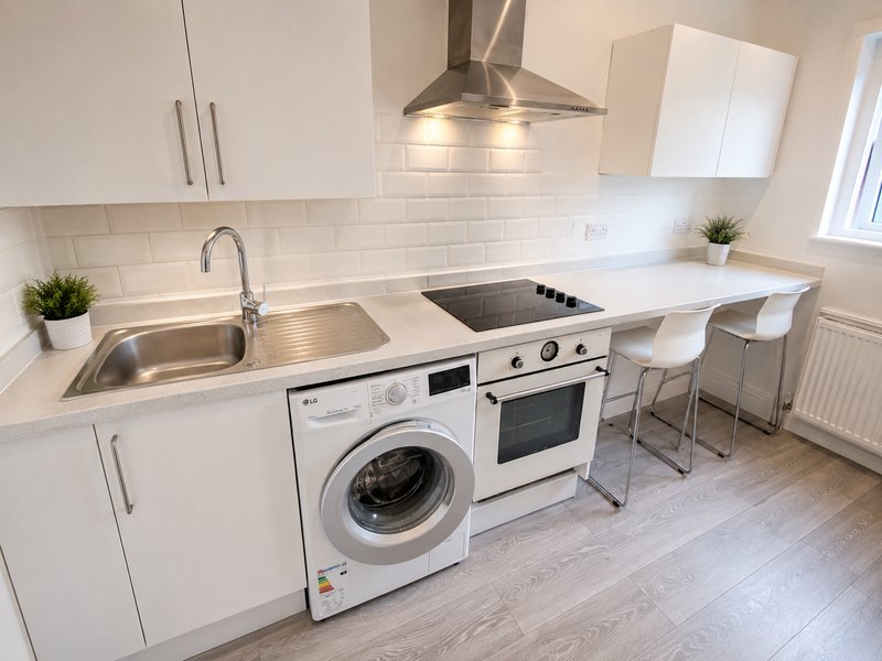 Modern white kitchen with appliances, sink, breakfast bar and bar stools