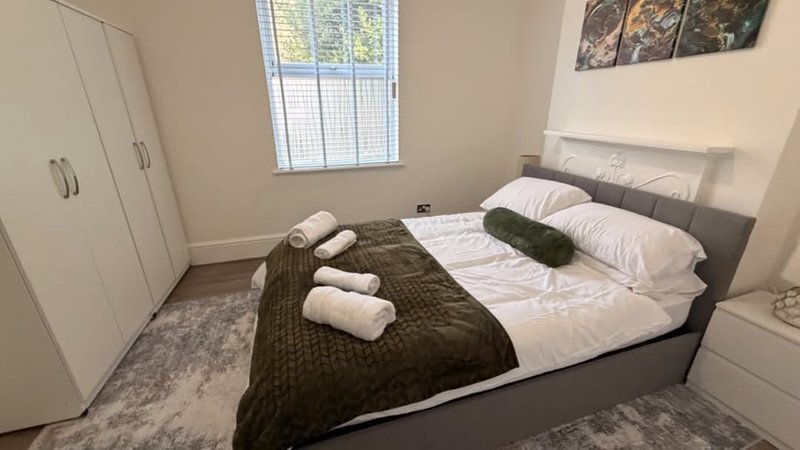 Modern bedroom with double bed, rolled towels, dark bedding, wardrobe and window