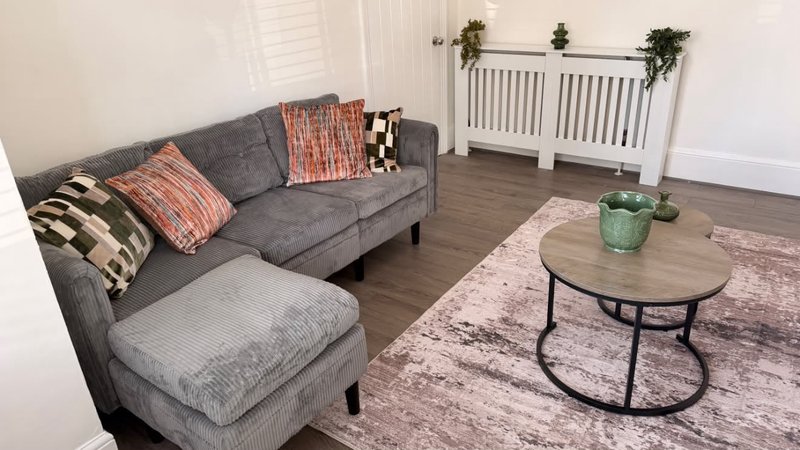 Living room with gray sectional sofa, patterned cushions, wooden oval coffee table, and potted plants
