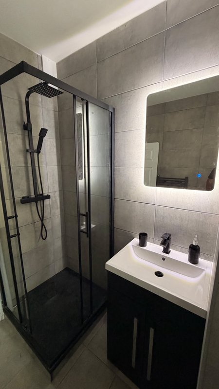 Modern bathroom with corner shower enclosure, wall-mounted sink, illuminated mirror and tiled walls