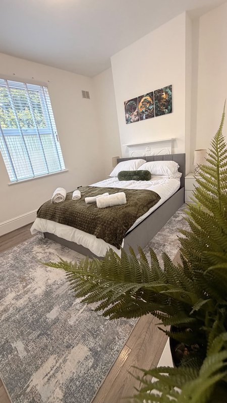 Bedroom with single bed, rolled towels, fern plant, and window with blinds