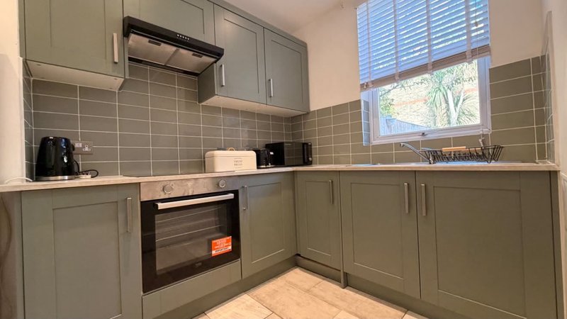 Modern kitchen with sage green cabinetry, integrated oven, wooden countertops and window