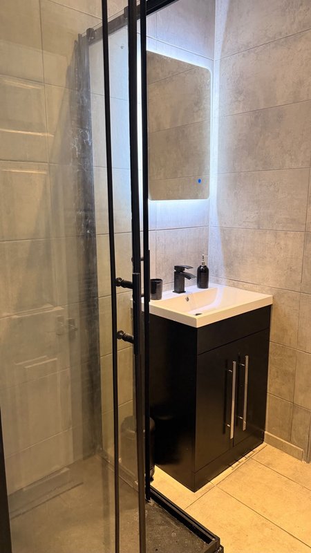 Modern bathroom with black vanity, glass shower enclosure, and tiled walls