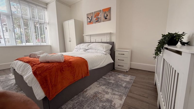 Modern bedroom with double bed, orange throw, bedside tables and window with shutters