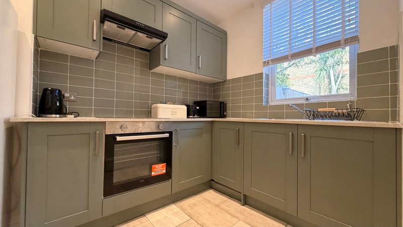 Modern kitchen with sage green cabinetry, black oven, and window with shutters