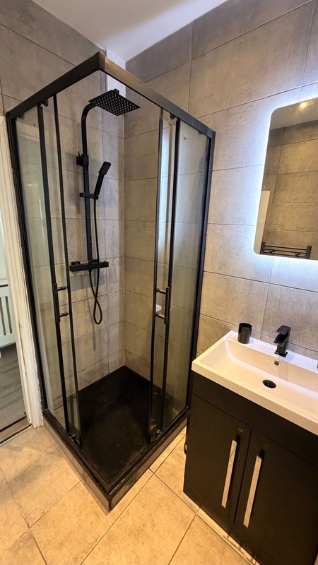 Modern bathroom with black-framed shower enclosure, vanity sink with mirror, and tiled walls