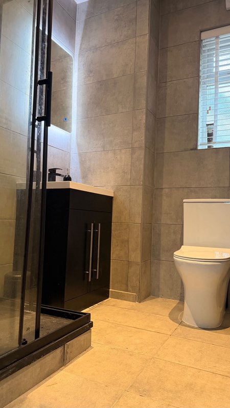 Modern bathroom with tiled walls, black vanity cabinet, toilet, and glass shower enclosure